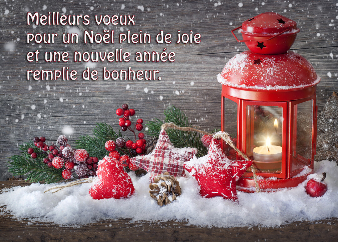 Une lanterne rouge illuminée repose dans la neige à côté de branches de sapin, de baies rouges et d'ornements traditionnels en tissu.