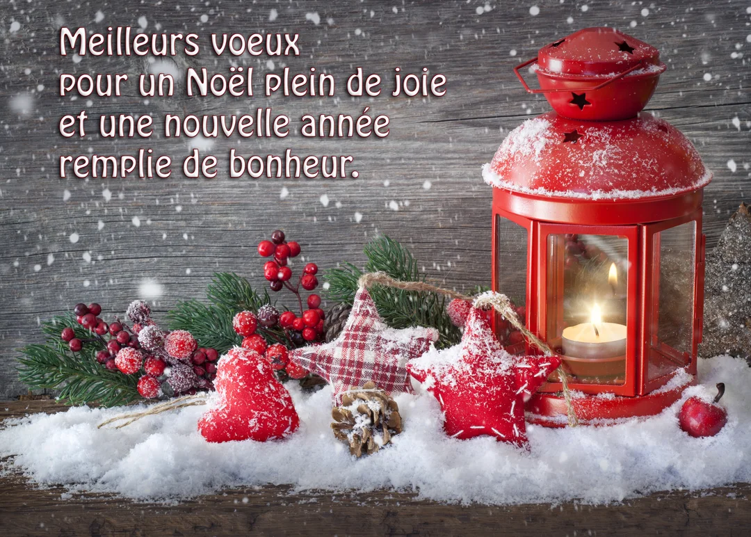 Une lanterne rouge illuminée repose dans la neige à côté de branches de sapin, de baies rouges et d'ornements traditionnels en tissu.