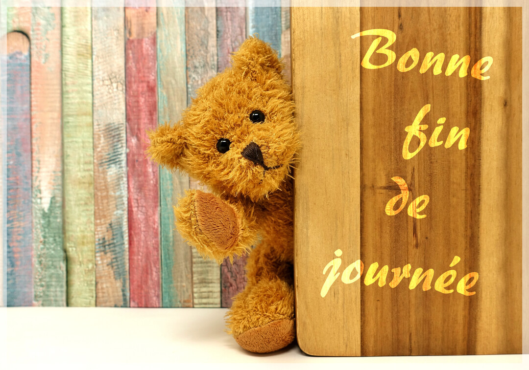 Un ours en peluche sourit et salue de la patte, émergeant de derrière une planche en bois sur un fond de lattes colorées.