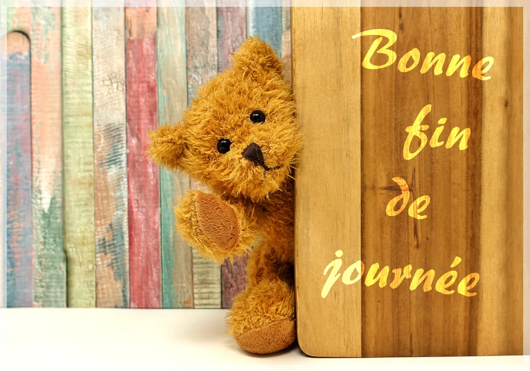 Un ours en peluche sourit et salue de la patte, émergeant de derrière une planche en bois sur un fond de lattes colorées.