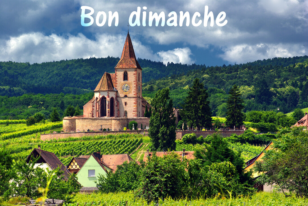 Une église en pierre avec un clocher pointu domine un village pittoresque niché au milieu de collines verdoyantes et de vignobles.