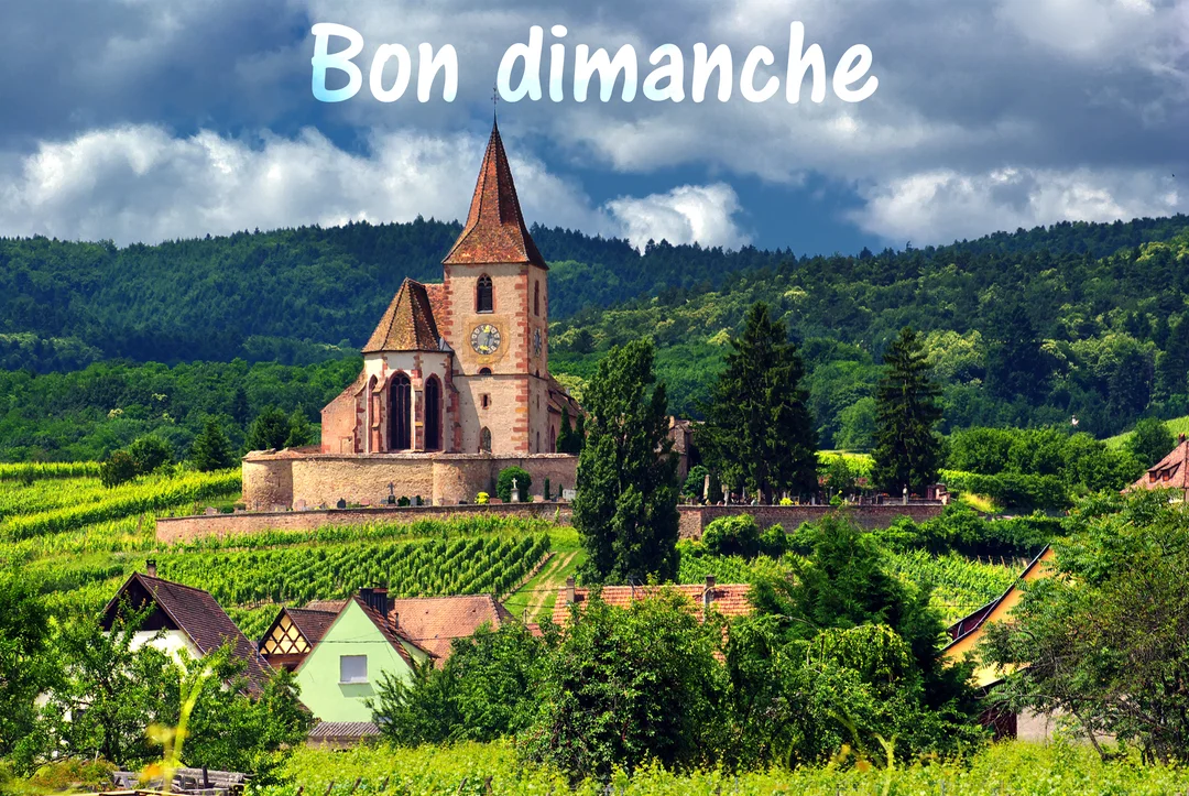 Une église en pierre avec un clocher pointu domine un village pittoresque niché au milieu de collines verdoyantes et de vignobles.