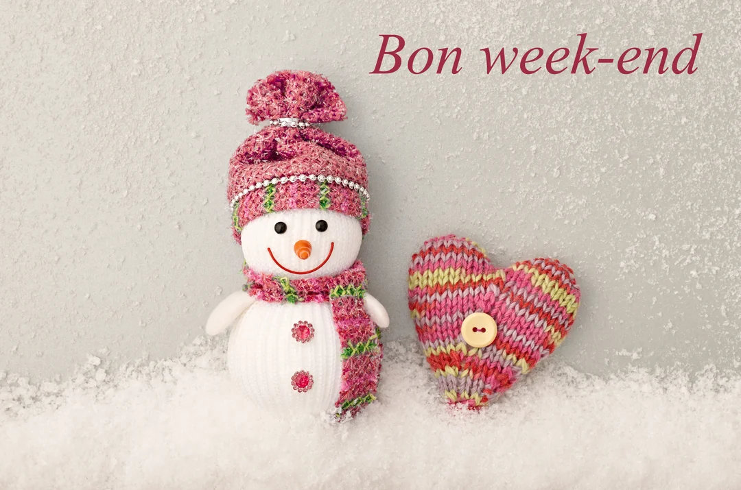 Un bonhomme de neige souriant en tissu, coiffé d'un bonnet rose, se tient dans la neige à côté d'un cœur en tricot multicolore.