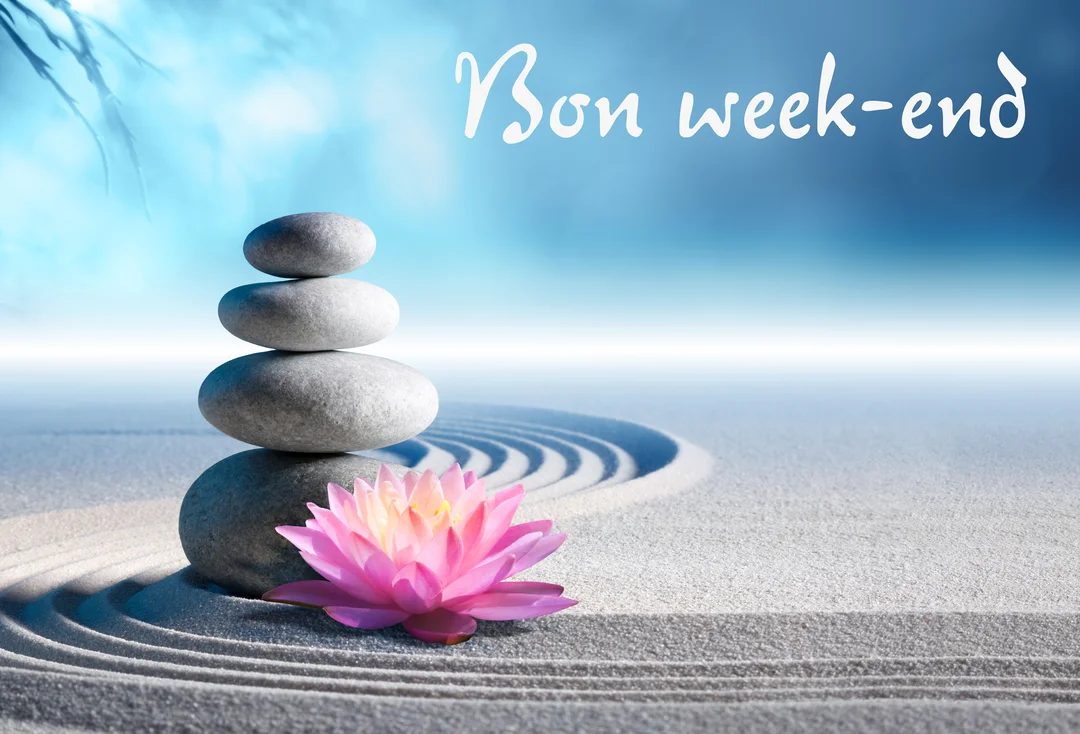 Une pile de quatre galets gris et une fleur de lotus rose reposent sur du sable blanc ratissé, sur un fond bleu et lumineux.