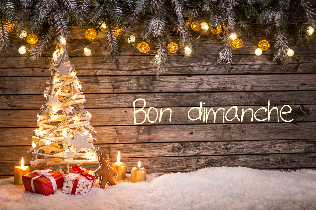 Une scène de Noël festive avec un sapin en bois illuminé, des cadeaux et bougies sur la neige devant un mur en bois.
