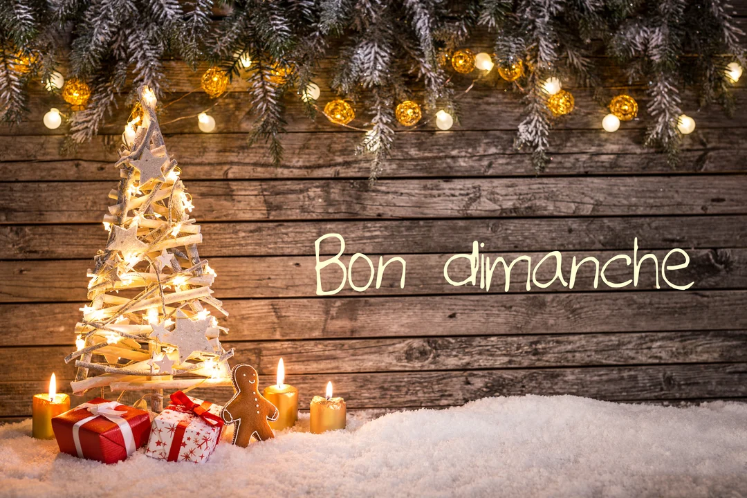 Une scène de Noël festive avec un sapin en bois illuminé, des cadeaux et bougies sur la neige devant un mur en bois.