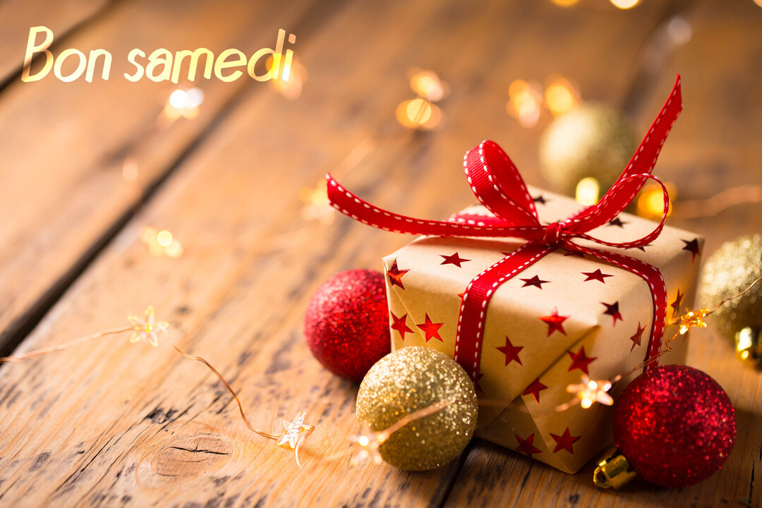 Un paquet cadeau décoré d'étoiles et d'un ruban rouge est posé sur du bois, entouré de boules de Noël et de lumières.