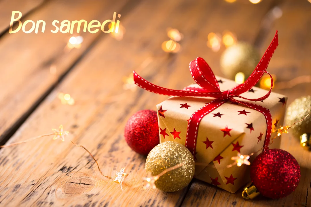 Un paquet cadeau décoré d'étoiles et d'un ruban rouge est posé sur du bois, entouré de boules de Noël et de lumières.