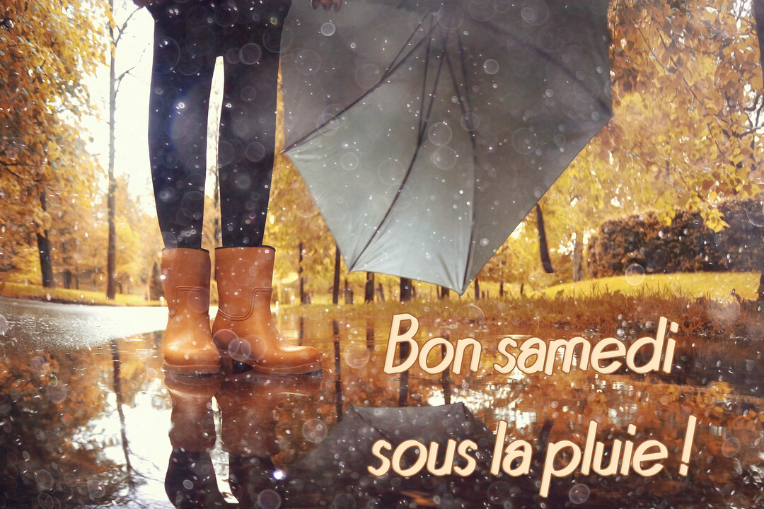 Vue en contre-plongée des jambes d'une personne portant des bottes de pluie, tenant un parapluie dans un parc automnal pluvieux avec reflets.