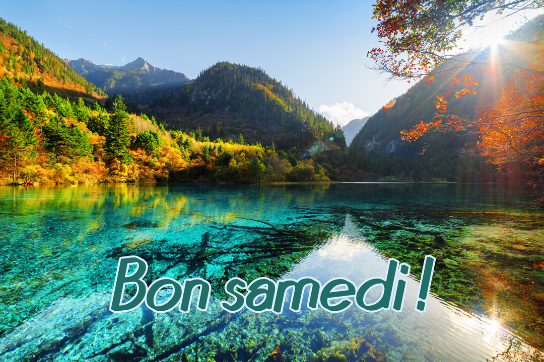 Un paysage de montagne avec un lac aux eaux turquoise cristallines reflétant les forêts automnales et un soleil éclatant dans un ciel bleu.