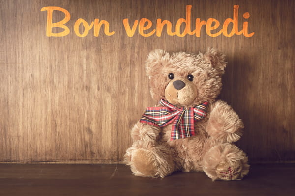 Un adorable ours en peluche marron avec un nœud papillon à carreaux, assis devant un fond en bois. Le texte 'Bon vendredi' est écrit au-dessus.