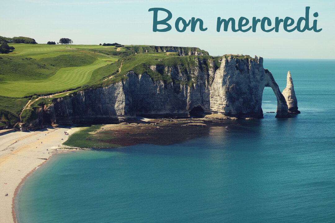 Vue aérienne des falaises d'Étretat en Normandie, avec ses arches naturelles plongeant dans une mer turquoise sous un ciel clair et ensoleillé.