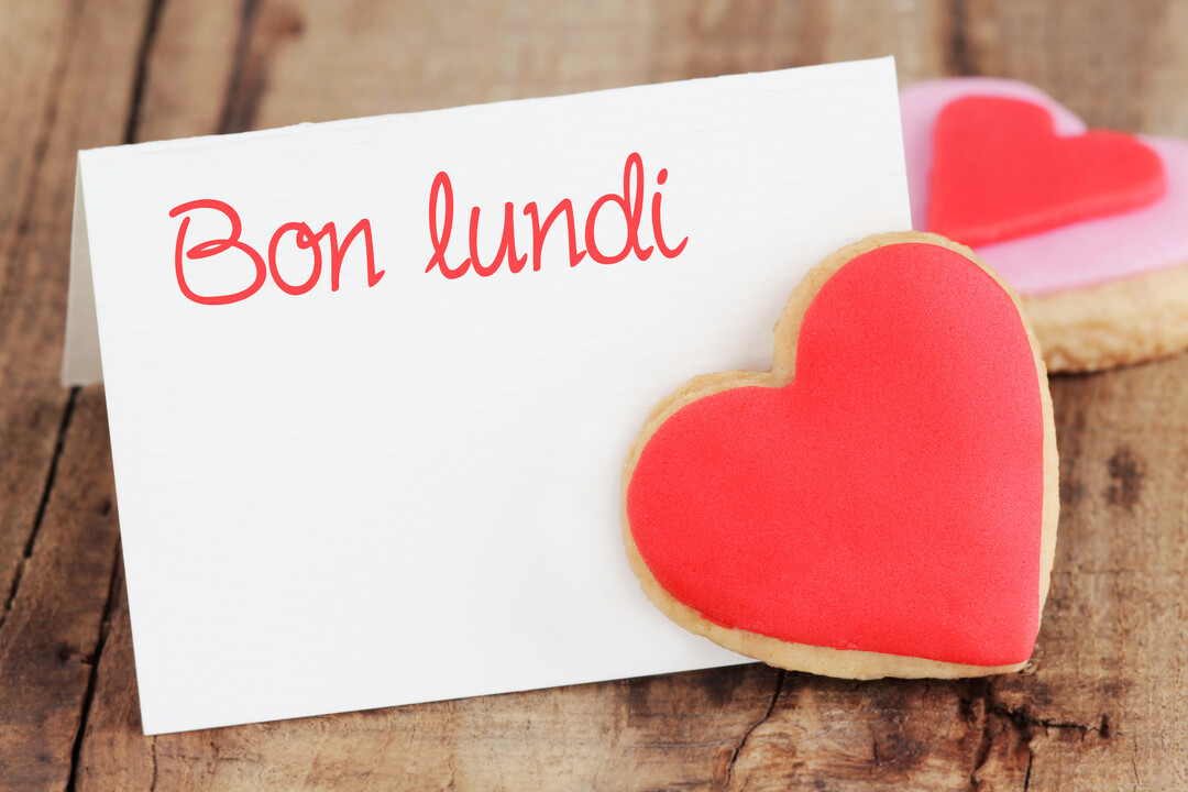 Une carte blanche avec l'inscription 'Bon lundi' en rouge, posée près de biscuits en forme de cœur sur une surface en bois rustique.