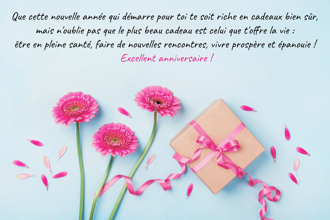 Sur un fond bleu pastel, trois gerberas roses sont disposés à côté d'une boîte cadeau nouée d'un ruban rose, avec des pétales éparpillés.