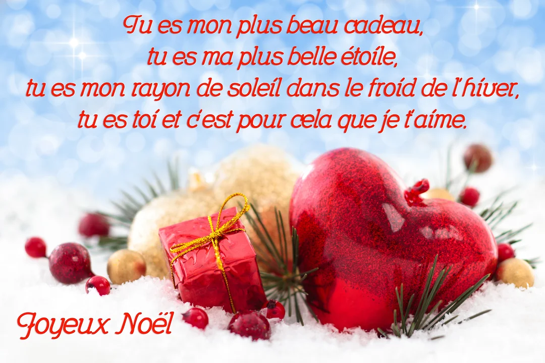Une scène de Noël enneigée avec un grand cœur rouge brillant, un petit cadeau et des boules dorées au premier plan.