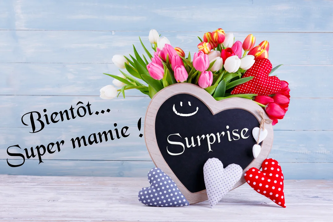 Une composition florale avec un bouquet de tulipes, des cœurs en tissu et une ardoise en cœur affichant le mot 'Surprise'.