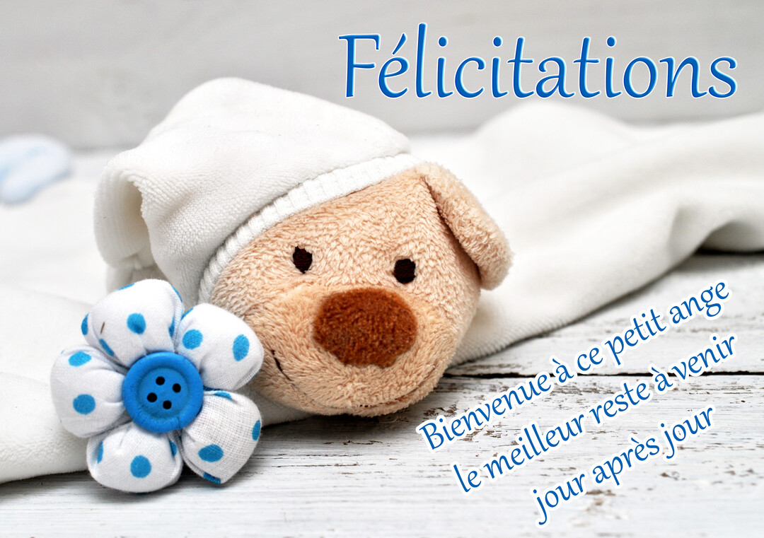 Un doudou ours en peluche beige avec un bonnet blanc est posé sur une couverture, à côté d'une fleur en tissu blanc et bleu.