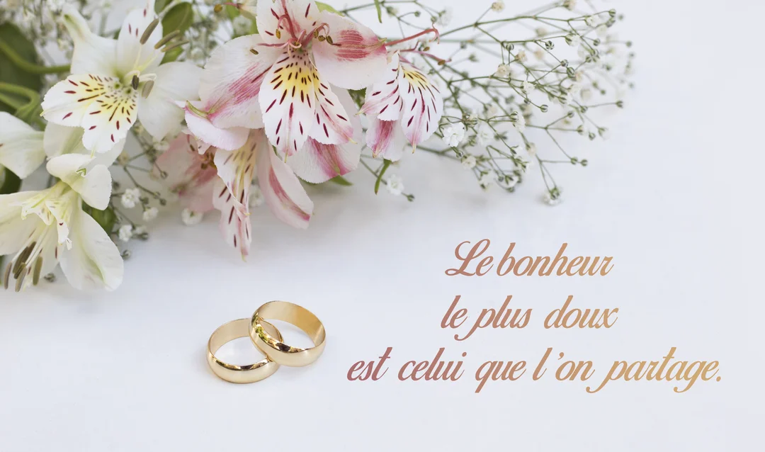 Sur un fond blanc, deux alliances dorées reposent à côté d'un bouquet d'alstroemerias et de gypsophiles, avec une citation sur le bonheur.