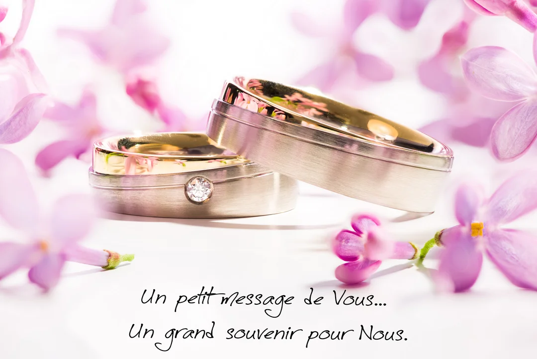 Gros plan sur deux alliances en argent et or posées sur une surface blanche, délicatement entourées de petites fleurs de lilas de couleur mauve.