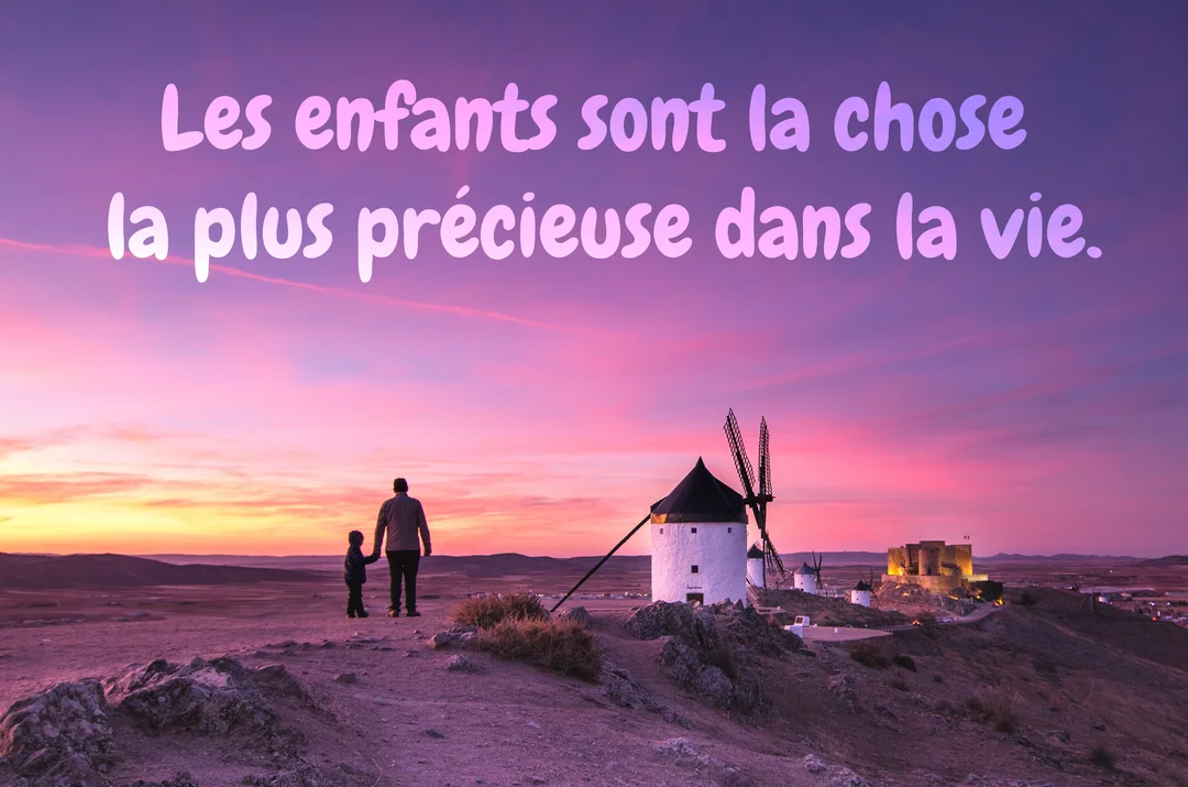 Un homme et un jeune garçon se tiennent la main sur une colline, regardant des moulins à vent sous un ciel violet au crépuscule.