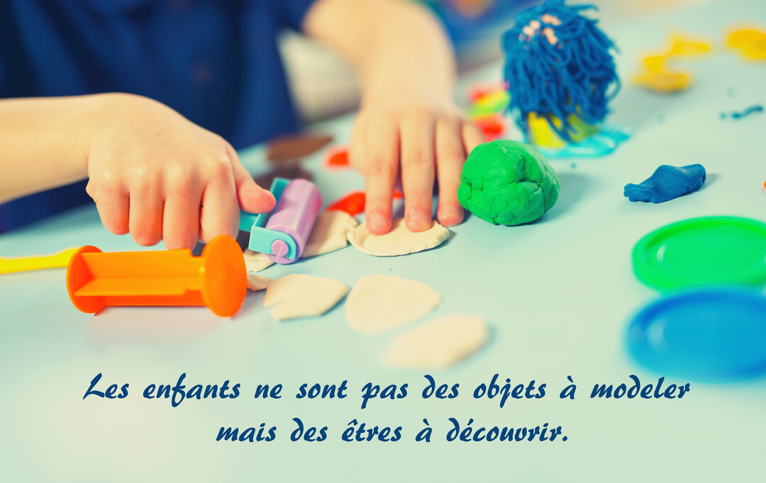 Gros plan sur les mains d'un enfant qui modèle de la pâte à modeler de différentes couleurs sur une table bleue.