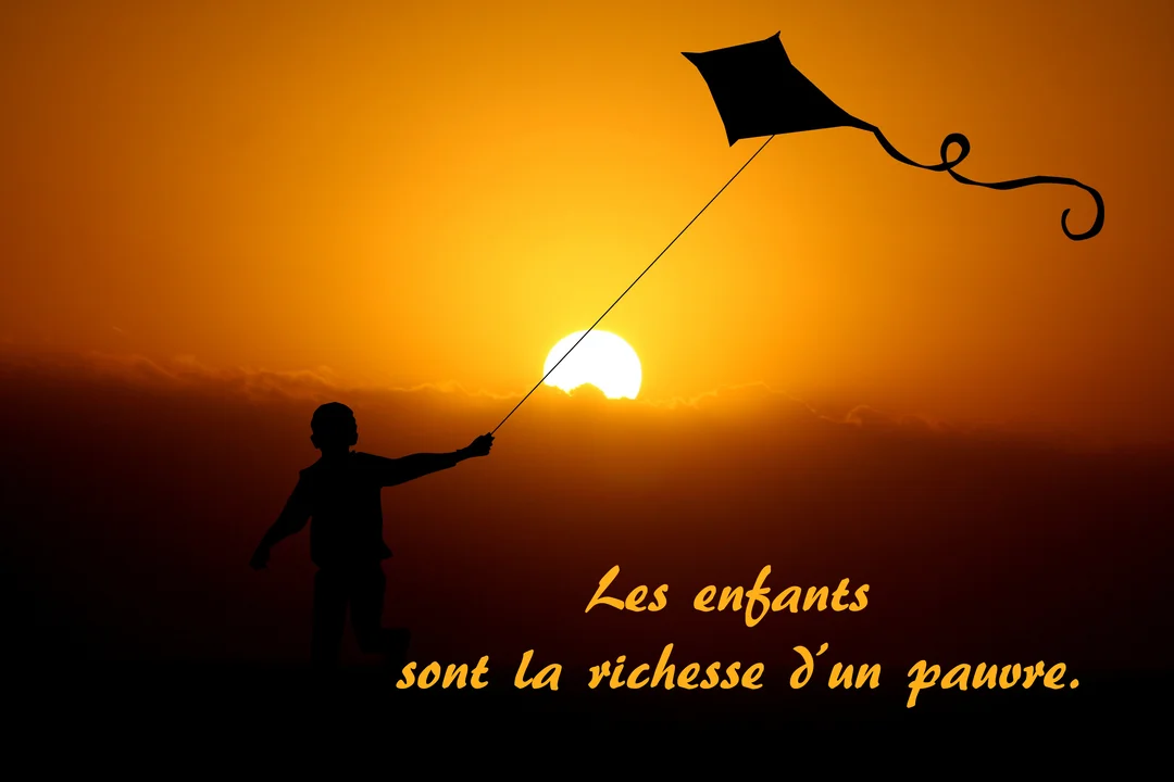 Une silhouette d'enfant tenant un cerf-volant se détache sur un ciel orangé éclatant lors d'un magnifique coucher de soleil.