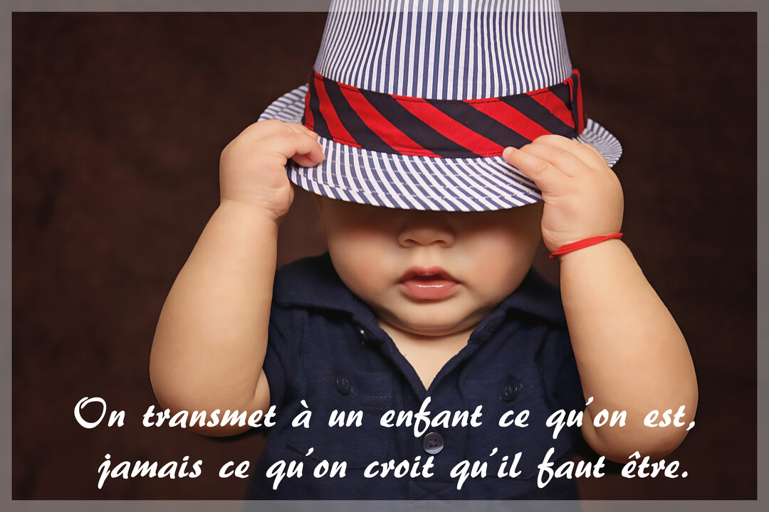 Un jeune enfant en polo bleu abaisse un chapeau à rayures sur ses yeux, avec un bracelet rouge au poignet, sur fond marron.
