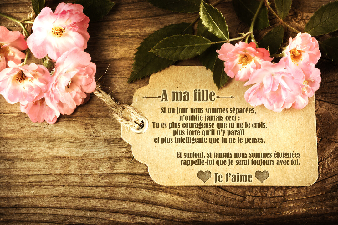 Sur un fond en bois, une étiquette en papier porte un message touchant, accompagnée de quelques roses roses et de leurs feuilles.