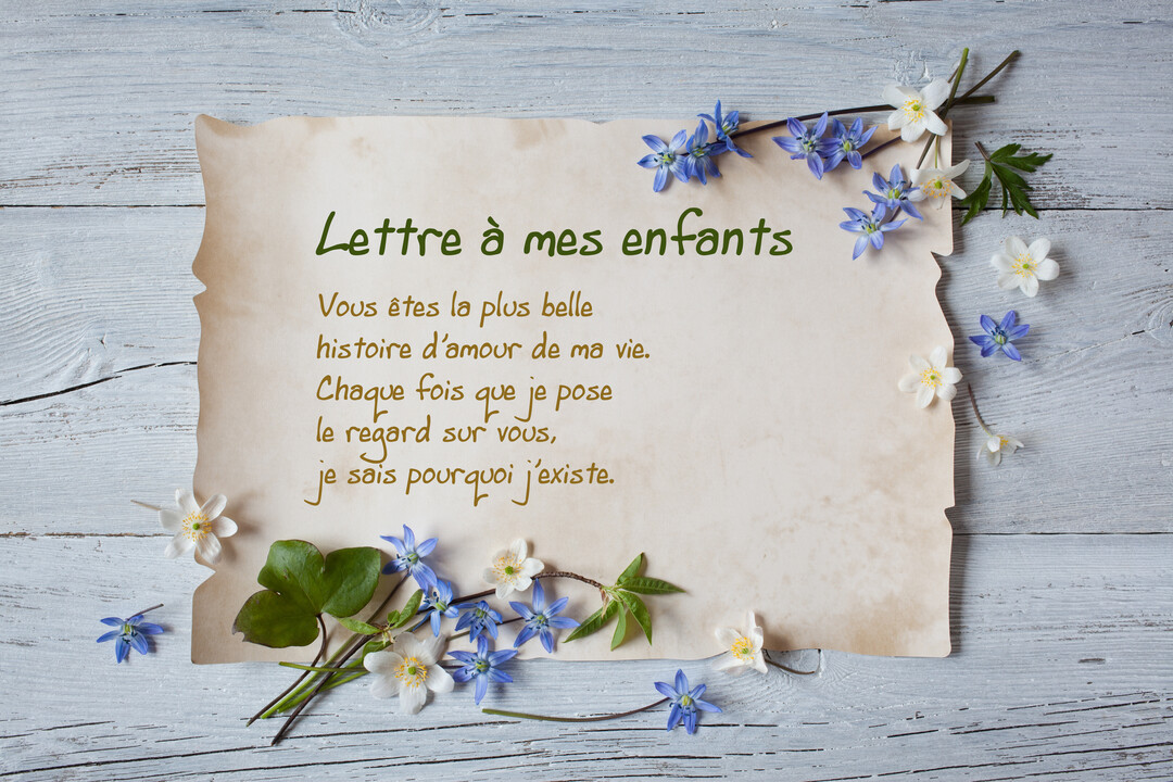 Un parchemin contenant une lettre d'amour à ses enfants est posé sur une surface en bois, entouré de petites fleurs bleues et blanches.