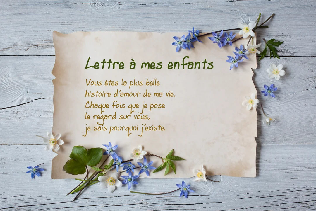 Un parchemin contenant une lettre d'amour à ses enfants est posé sur une surface en bois, entouré de petites fleurs bleues et blanches.