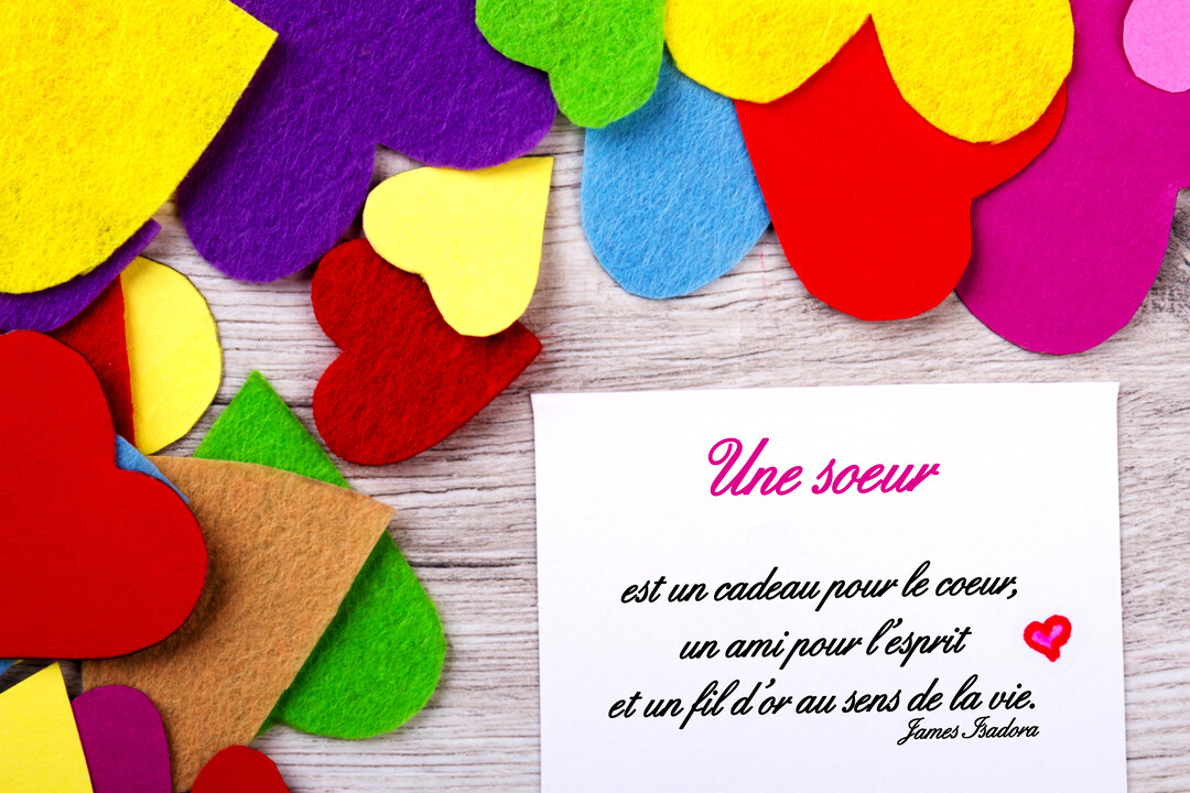 Sur un fond de bois clair, une carte blanche porte une citation sur les soeurs, entourée de coeurs multicolores en feutrine.