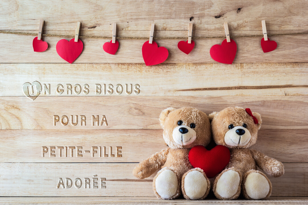 Deux adorables oursons en peluche bruns sont assis côte à côte devant un fond en bois, tenant un cœur rouge entre eux.