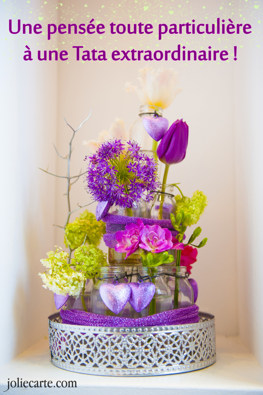 Une composition florale sophistiquée avec des fleurs violettes et blanches dans des bocaux en verre, décorée de cœurs et de rubans pailletés.