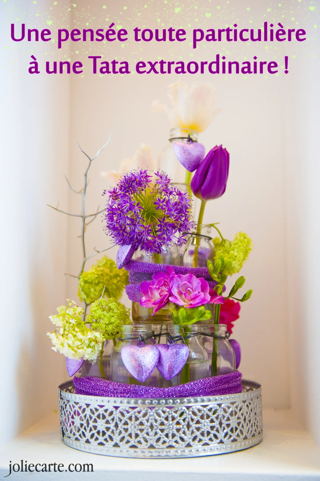 Une composition florale sophistiquée avec des fleurs violettes et blanches dans des bocaux en verre, décorée de cœurs et de rubans pailletés.