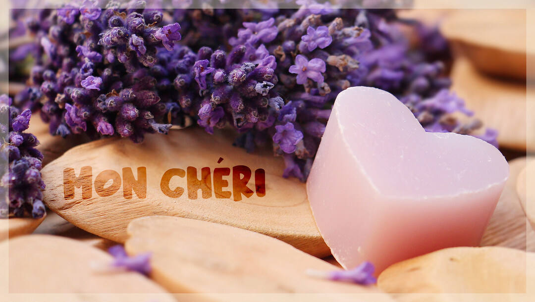 Gros plan sur un savon rose en forme de cœur et des brins de lavande, avec l'inscription 'Mon chéri' sur une pièce de bois.