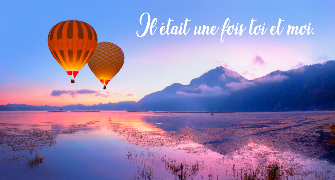 Deux montgolfières illuminées s'élèvent au-dessus d'un lac miroitant, face à des montagnes brumeuses sous un ciel aux teintes de crépuscule.