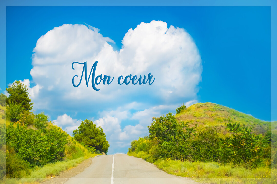 Paysage estival avec une route bordée de collines vertes, sous un ciel bleu où un grand nuage blanc forme un cœur parfait.