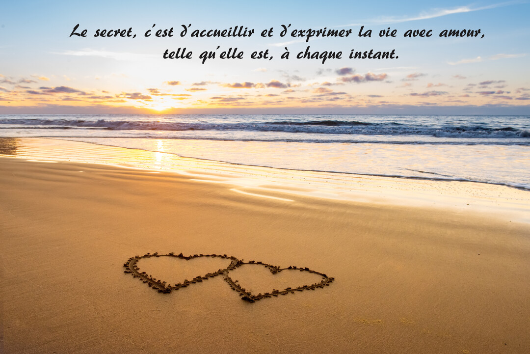 Sur une plage au coucher du soleil, deux cœurs entrelacés sont dessinés dans le sable mouillé, avec les vagues de l'océan en arrière-plan.