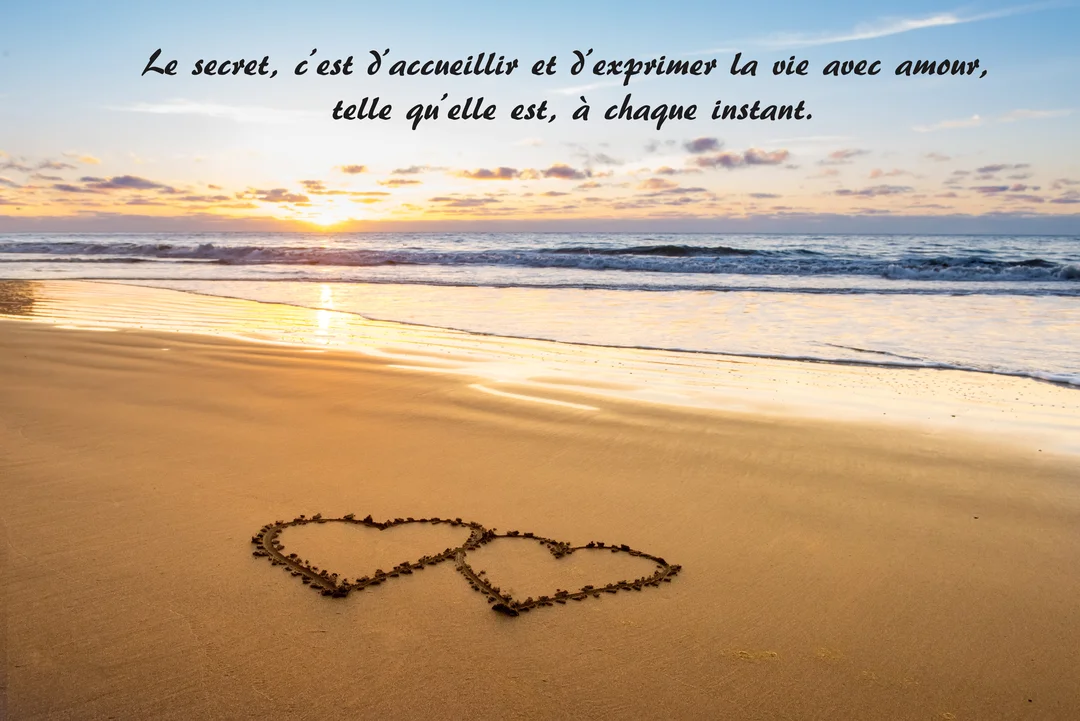 Sur une plage au coucher du soleil, deux cœurs entrelacés sont dessinés dans le sable mouillé, avec les vagues de l'océan en arrière-plan.