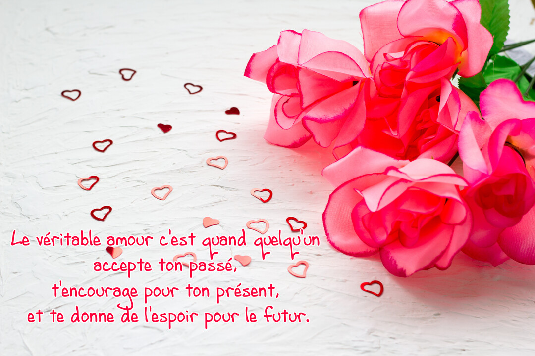 Sur un fond blanc texturé, des roses artificielles roses accompagnent une citation d'amour et des confettis en forme de cœurs rouges et roses.