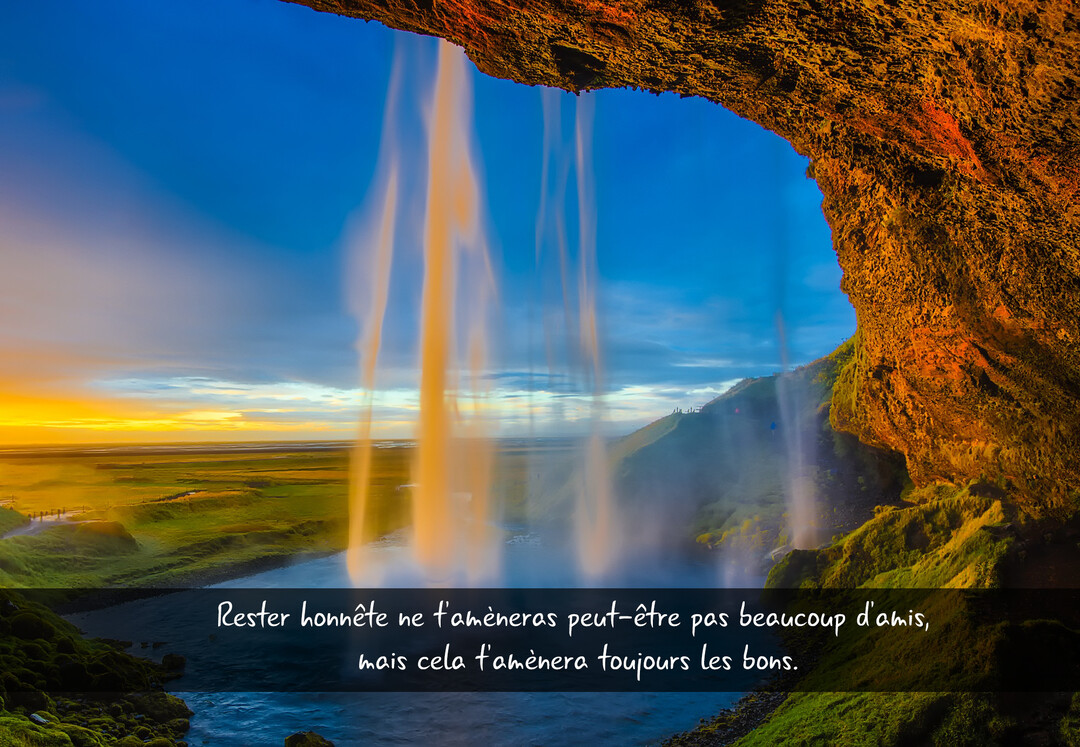 Vue depuis une grotte rocheuse derrière une cascade, regardant un paysage verdoyant et un ciel bleu et orangé au crépuscule.