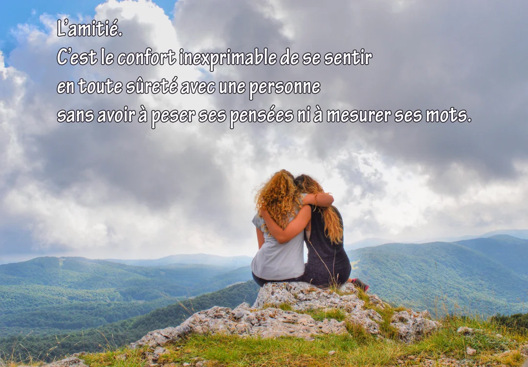 Deux jeunes femmes, vues de dos, s'enlacent en étant assises sur un rocher, contemplant un panorama de montagnes sous un ciel nuageux.