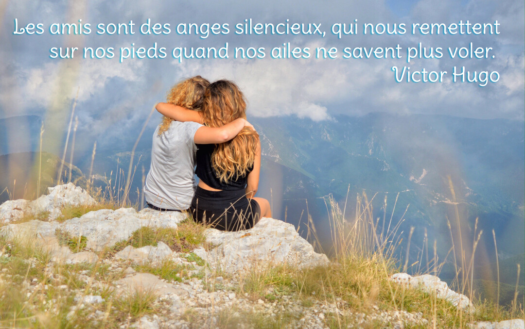 Deux femmes de dos, assises sur un rocher, s'enlacent en regardant un panorama montagneux sous un ciel nuageux.