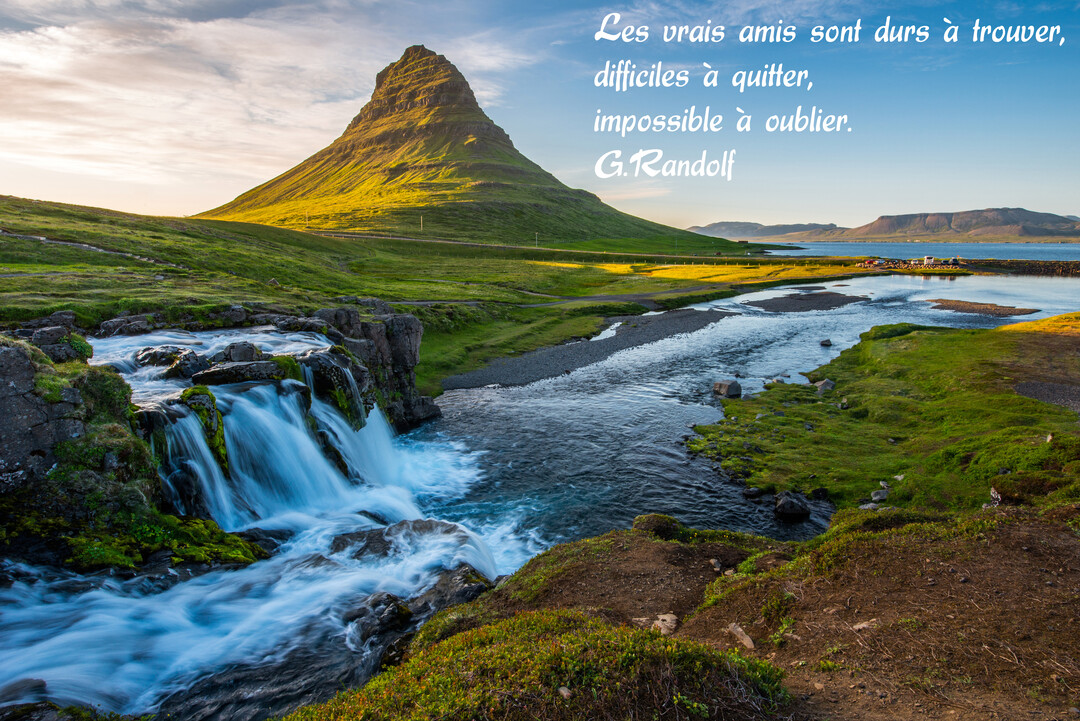Un paysage naturel spectaculaire en Islande, avec une montagne iconique, une cascade en premier plan et un cours d'eau sous un ciel lumineux.