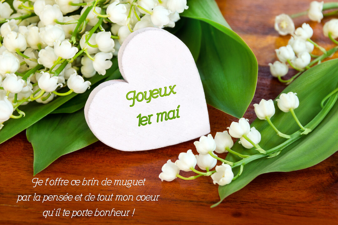 Une composition florale de brins de muguet avec leurs clochettes blanches et feuilles vertes, à côté d'un cœur blanc en bois.