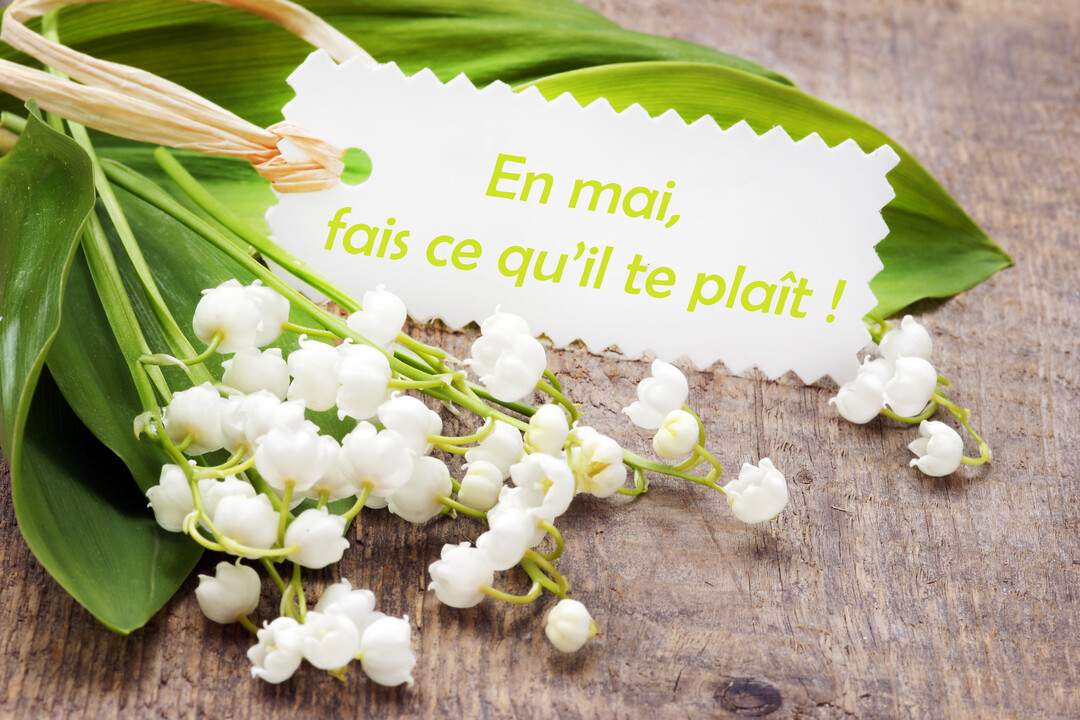 Un bouquet de muguet avec ses clochettes blanches et ses feuilles vertes est posé sur une surface en bois rustique avec une petite étiquette.