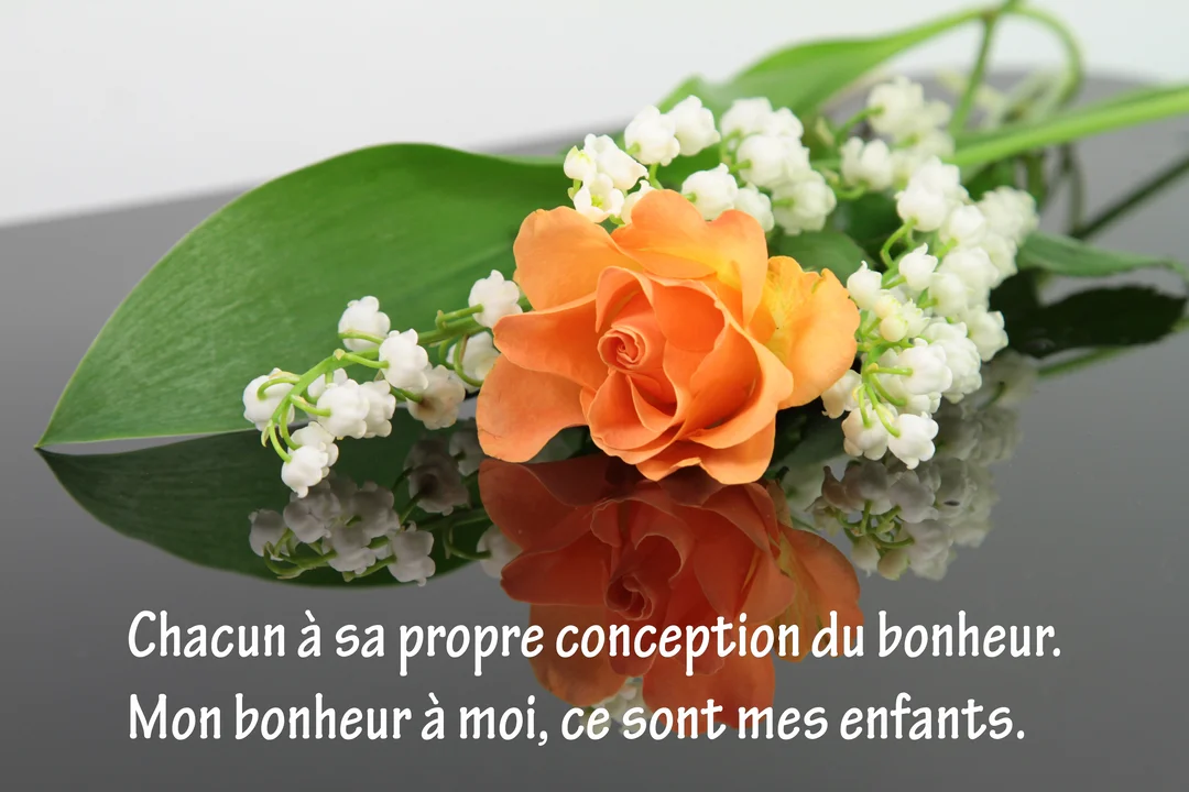 Une composition florale présentant une rose orange et du muguet blanc, posée sur une surface sombre qui reflète délicatement les fleurs.