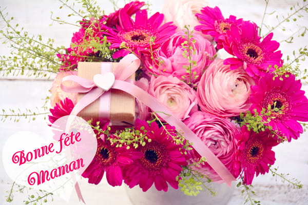 Carte de Fête des Mères avec un magnifique bouquet de gerberas et renoncules roses, un petit cadeau, et le texte "Bonne fête maman" dans un cœur.