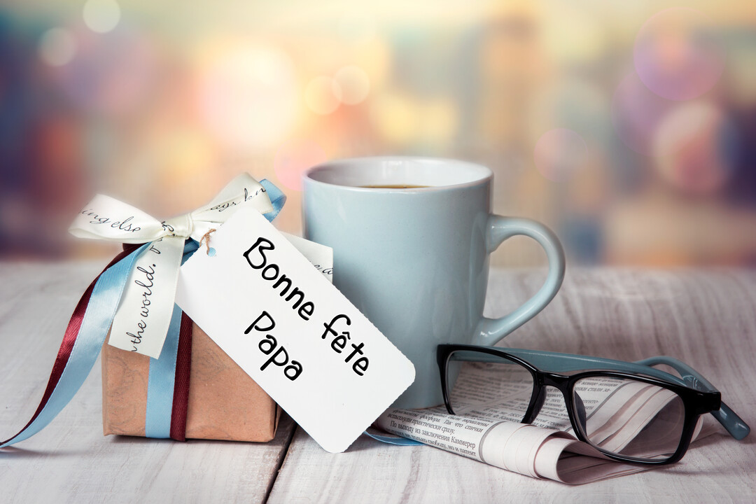 Une nature morte pour la fête des Pères avec un petit cadeau, une tasse de café, des lunettes et un journal sur une table en bois.