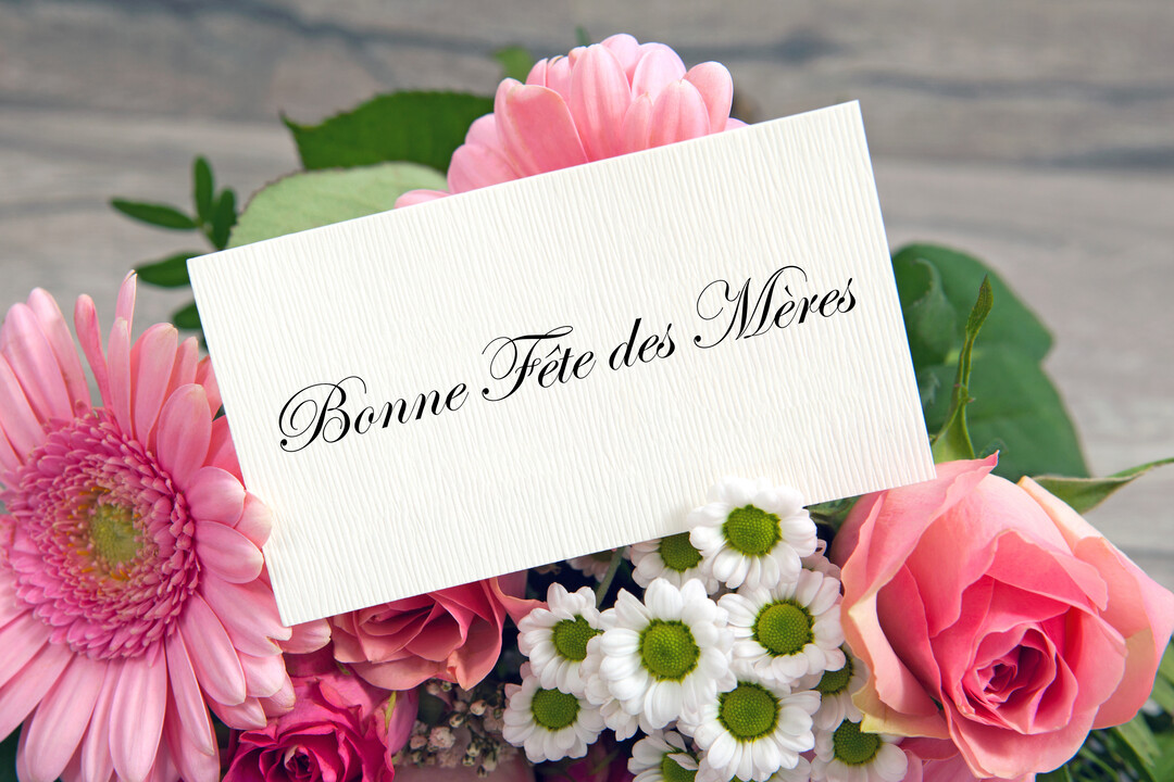 Une carte de vœux blanche avec l'inscription 'Bonne Fête des Mères' est posée sur un bouquet de fleurs fraîches roses et blanches.